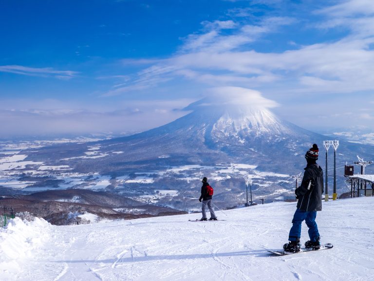 Snowboarder,and,skier,looking,at,snowy,volcano,with,cap,cloud